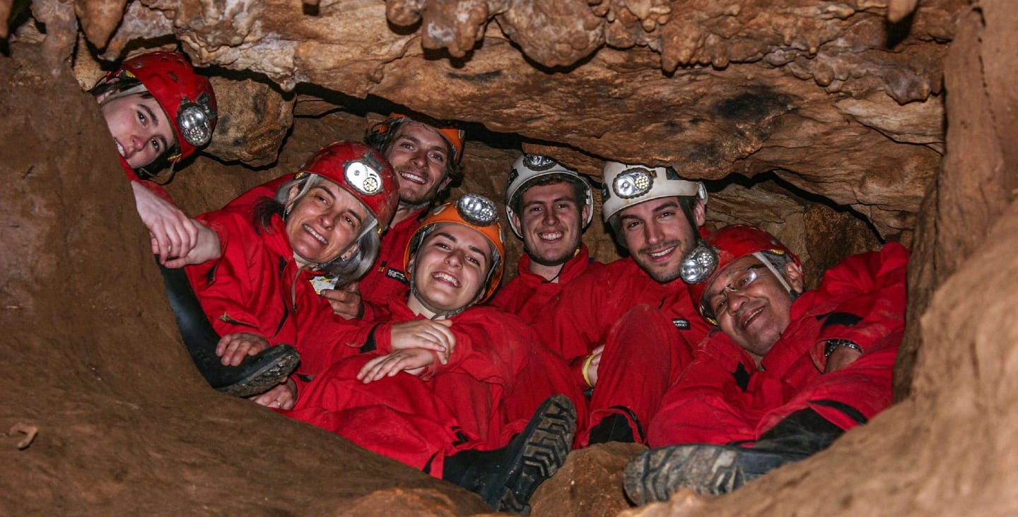 Group wearing red protective suits and illuminated helmets in an underground passage.