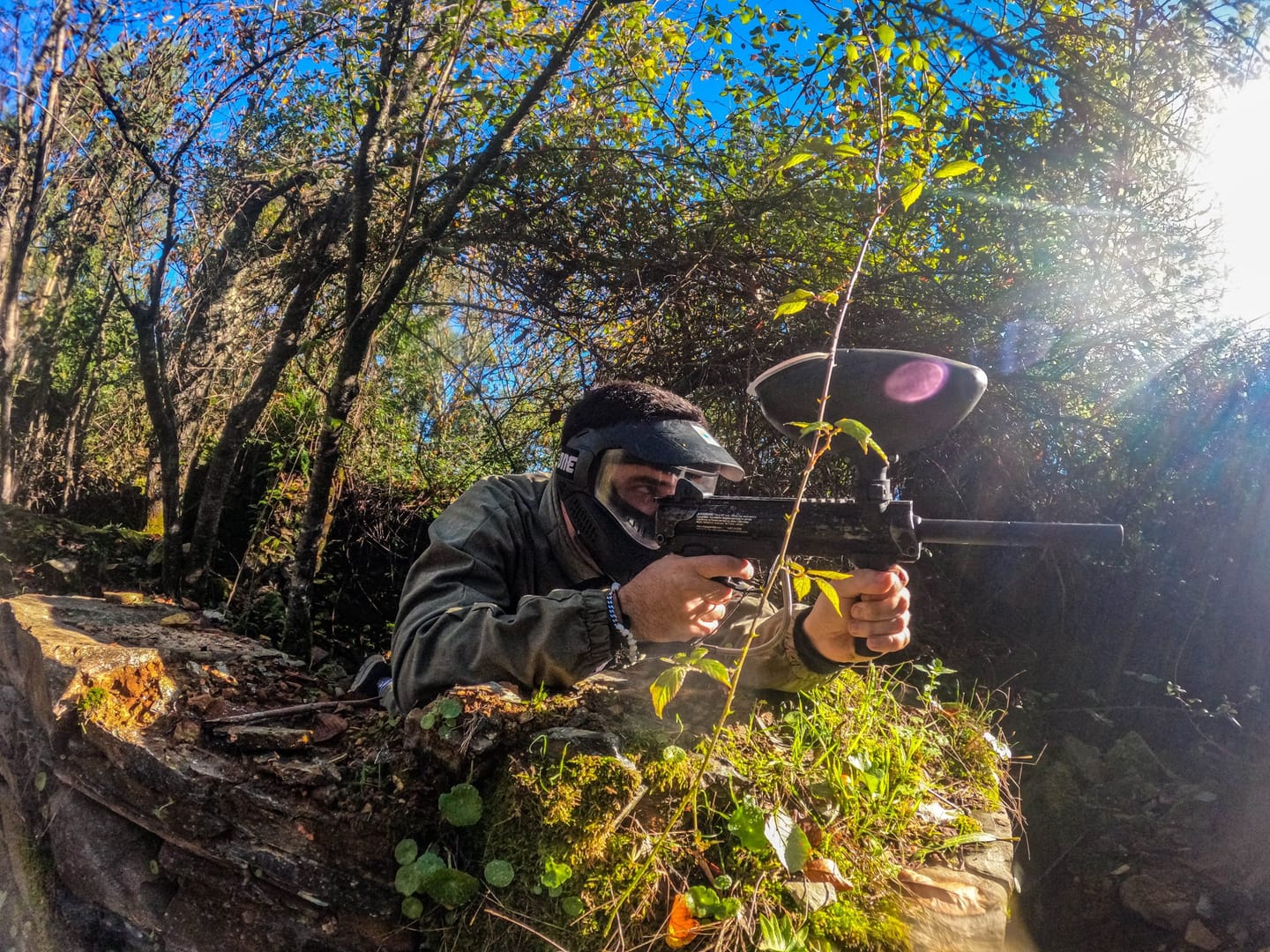 Participant with a mask and paintball marker among trees